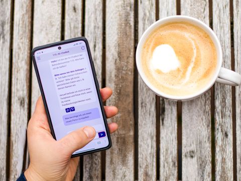 Smartphone mit KI-Chatbot neben einer Kaffeetasse