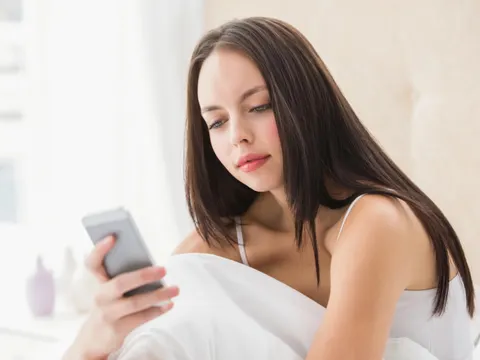 Brünettes Mädchen schickt einen Text auf dem Bett